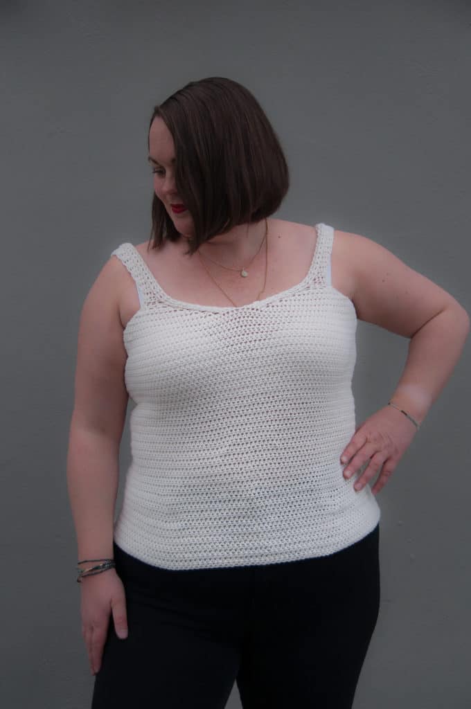 White crochet tank top made with a simple stitch pattern, worn against a plain gray background.