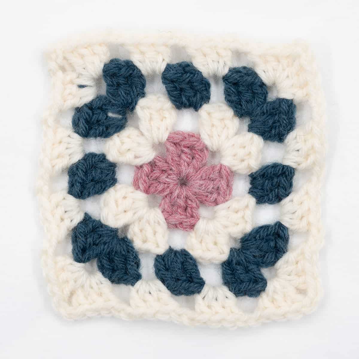 A crocheted granny square in white, blue and pink.