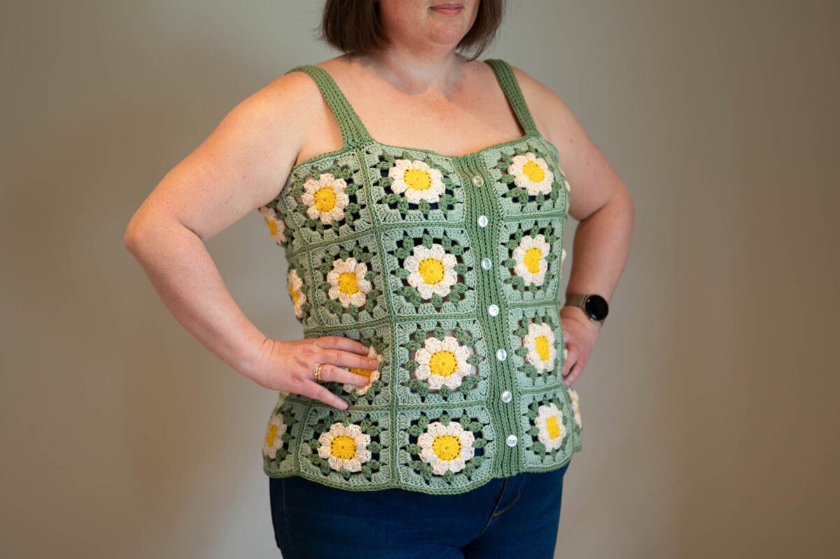 Crochet tank top made of granny squares in sunflower, oatmilk, sage, and misty green with white buttons down the front.